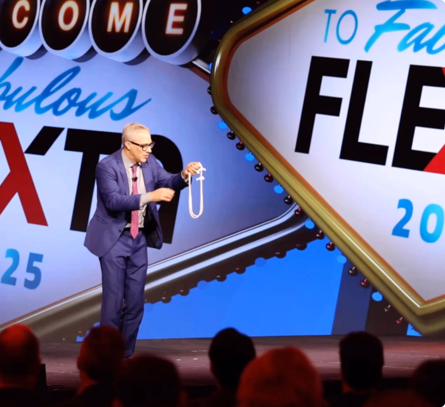 Speaker on stage at Flex Technology Group's 2025 event, in front of a Las Vegas style welcome sign